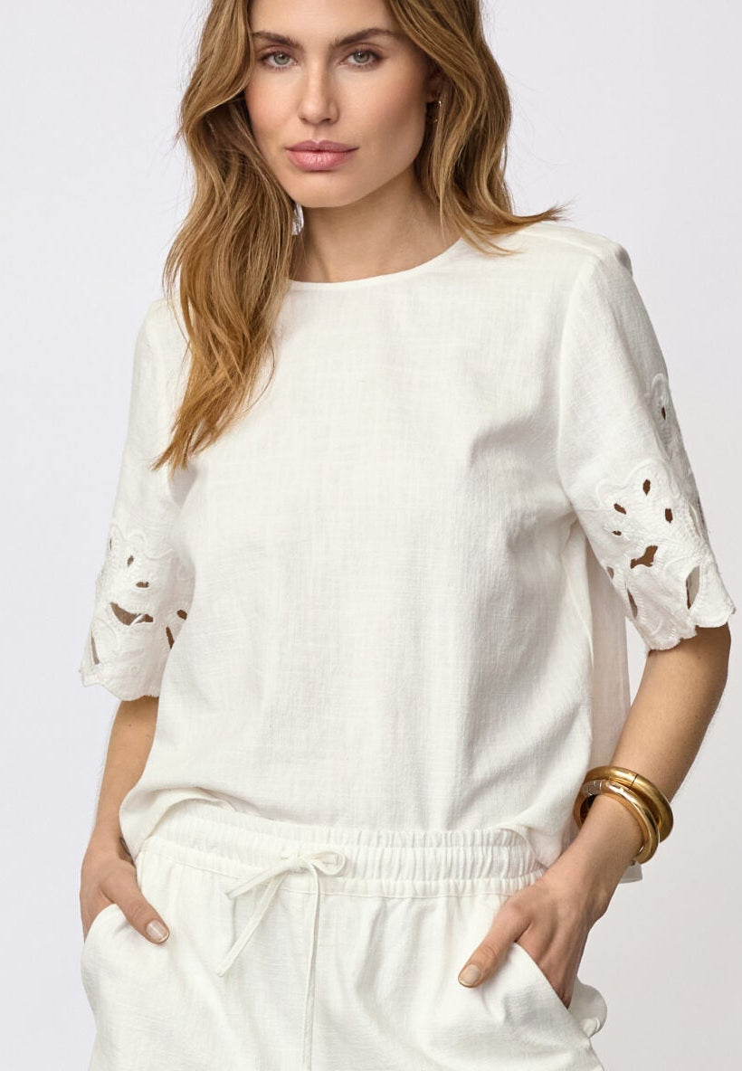Woman wearing a white outfit with lace details and brown knee-high boots on a plain background